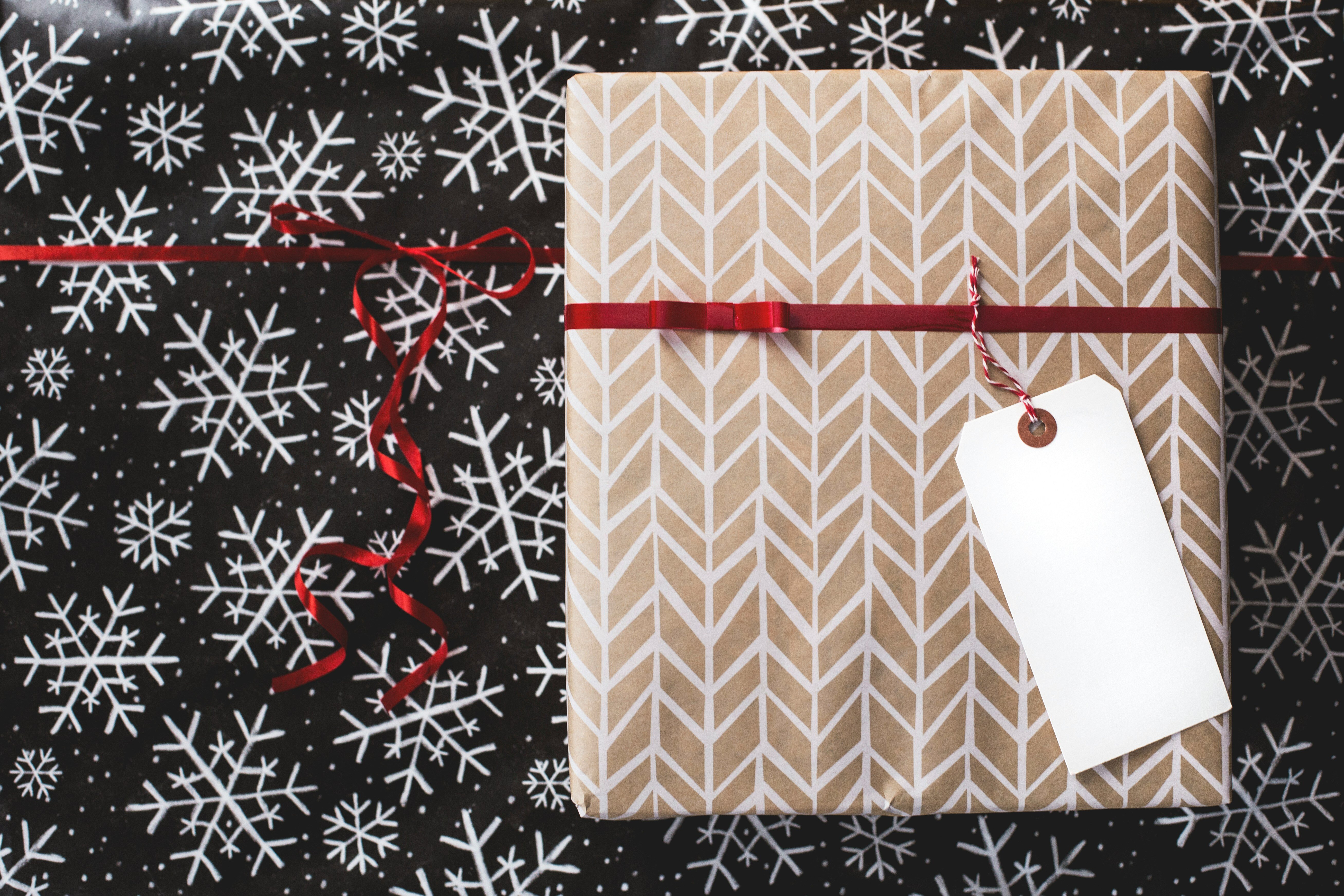 A gift wrapped in brown paper with a white pattern sits on a background of artistic snowflakes.